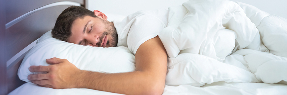 Man peacefully sleeping in bed under a white comforter