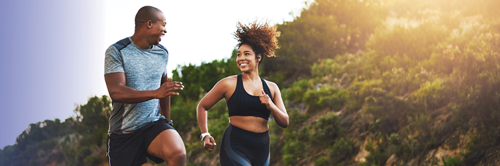 Smiling man and woman running outdoors in athletic wear on a sunny day